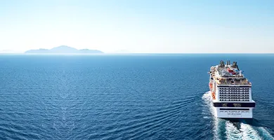 晴れた青空の下広い海を航行する大型クルーズ船。遠くの地平線には島が見える。